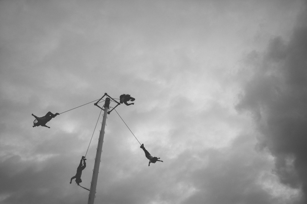 4 people hanging from a. swing which is a ride in an amusement park